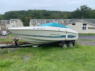 An older deck boat. It looks clean. It's white with styling blue lines running across it and a bright cyan canvas cover.